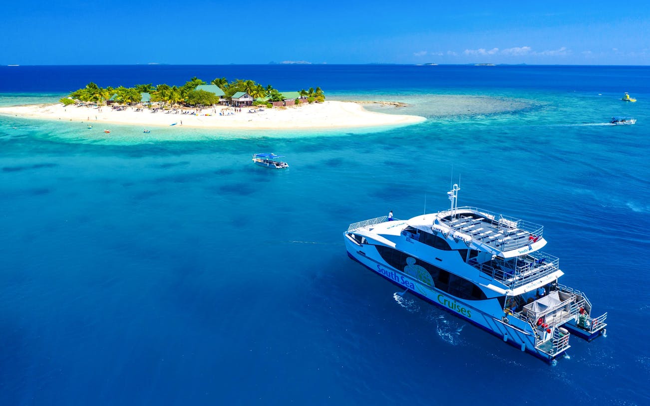 Cruise ship near South Sea Island, Fiji, with beach and palm trees in view.