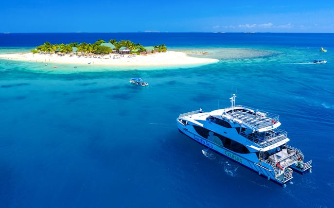 Cruise ship near South Sea Island, Fiji, with beach and palm trees in view.