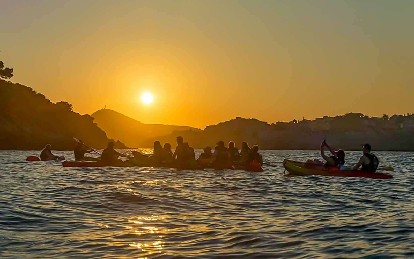 Kayakers paddling at sunset near Dubrovnik coastline.