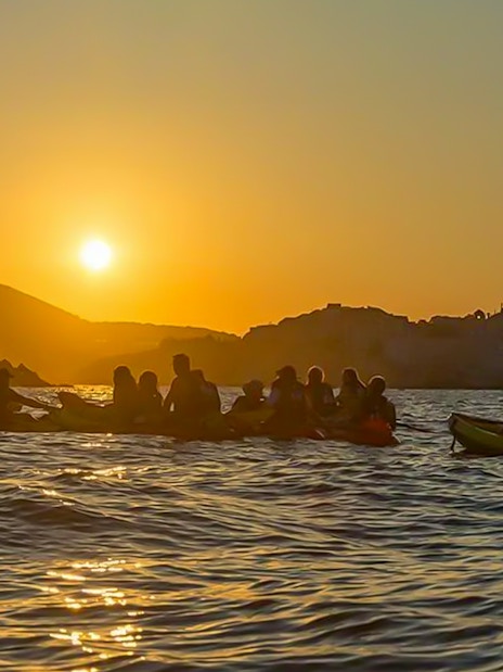 Kayakers paddling at sunset near Dubrovnik coastline.
