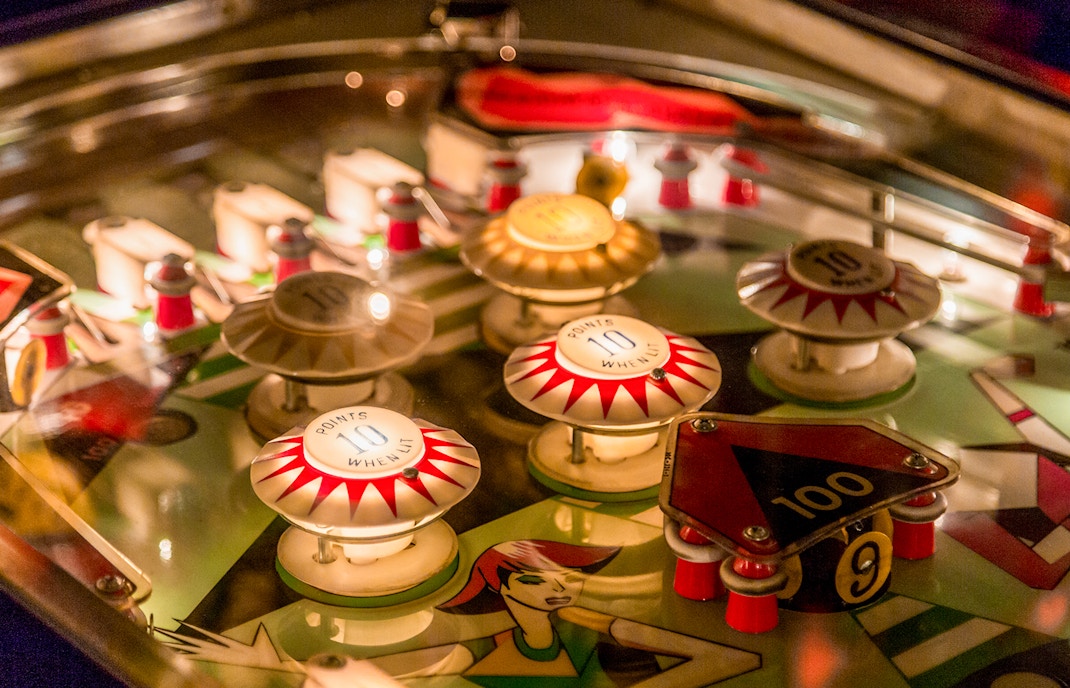 Vintage pinball machine with illuminated bumpers and flippers in a retro arcade setting.