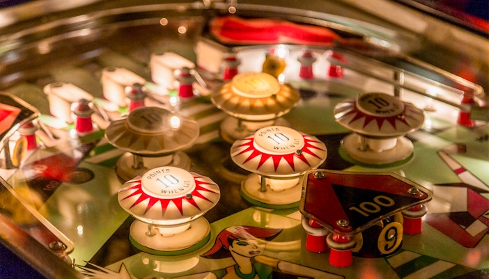 Vintage pinball machine with illuminated bumpers and flippers in a retro arcade setting.
