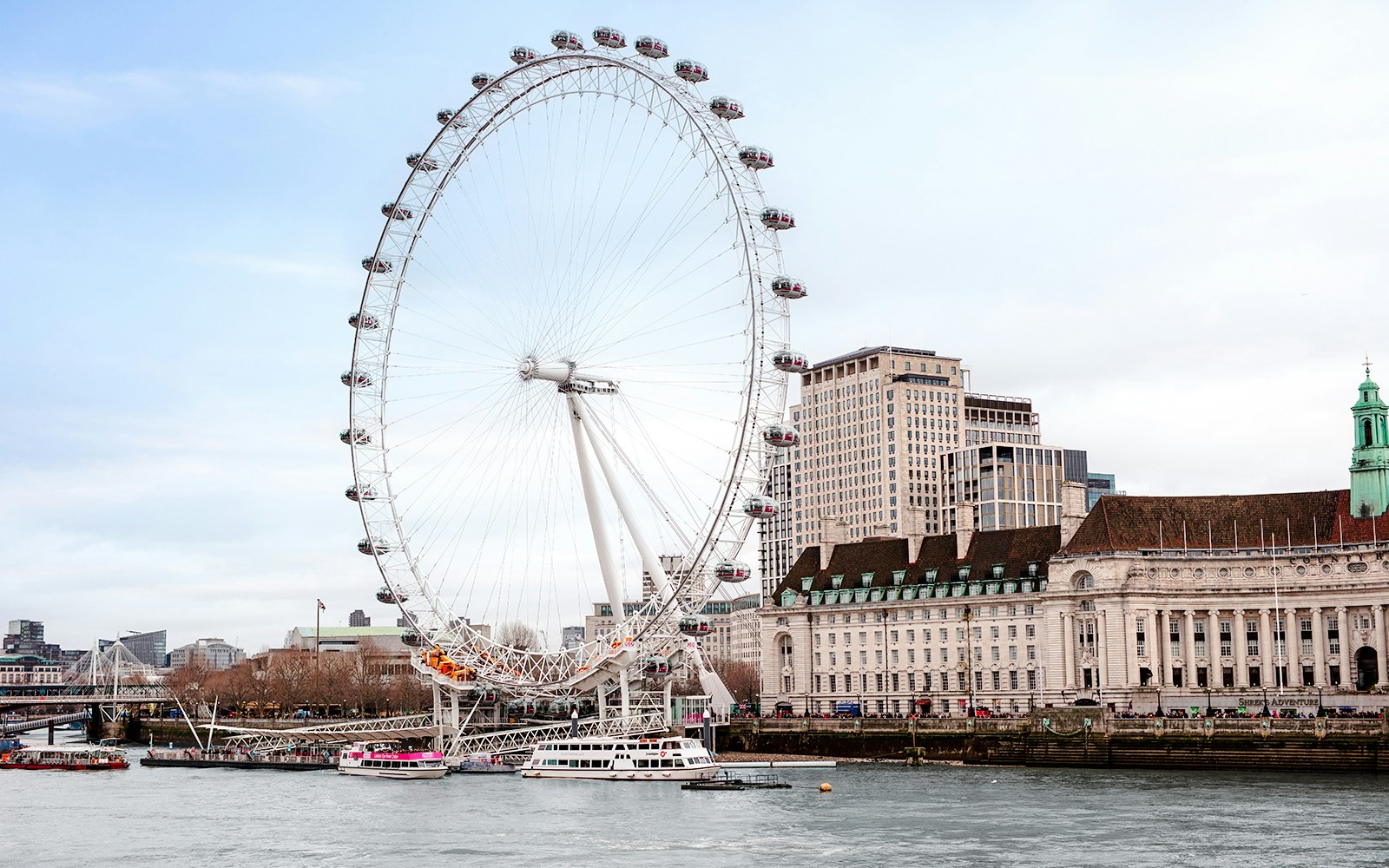 London Eye on the Thames River with nearby historic buildings.