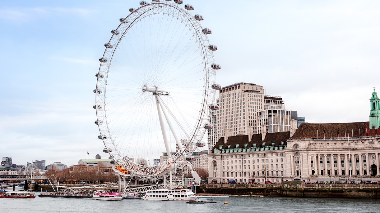 London Eye on the Thames River with nearby historic buildings.