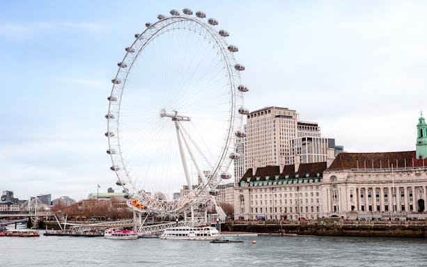 London Eye on the Thames River with nearby historic buildings.