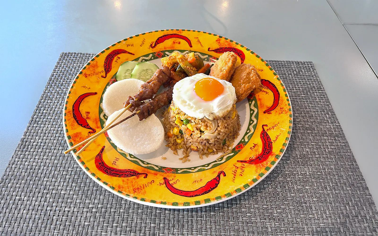 Fried rice with egg, satay skewers, and sides on a colorful plate onboard the yacht.