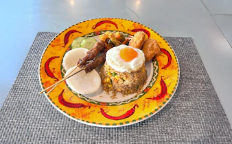 Fried rice with egg, satay skewers, and sides on a colorful plate onboard the yacht.