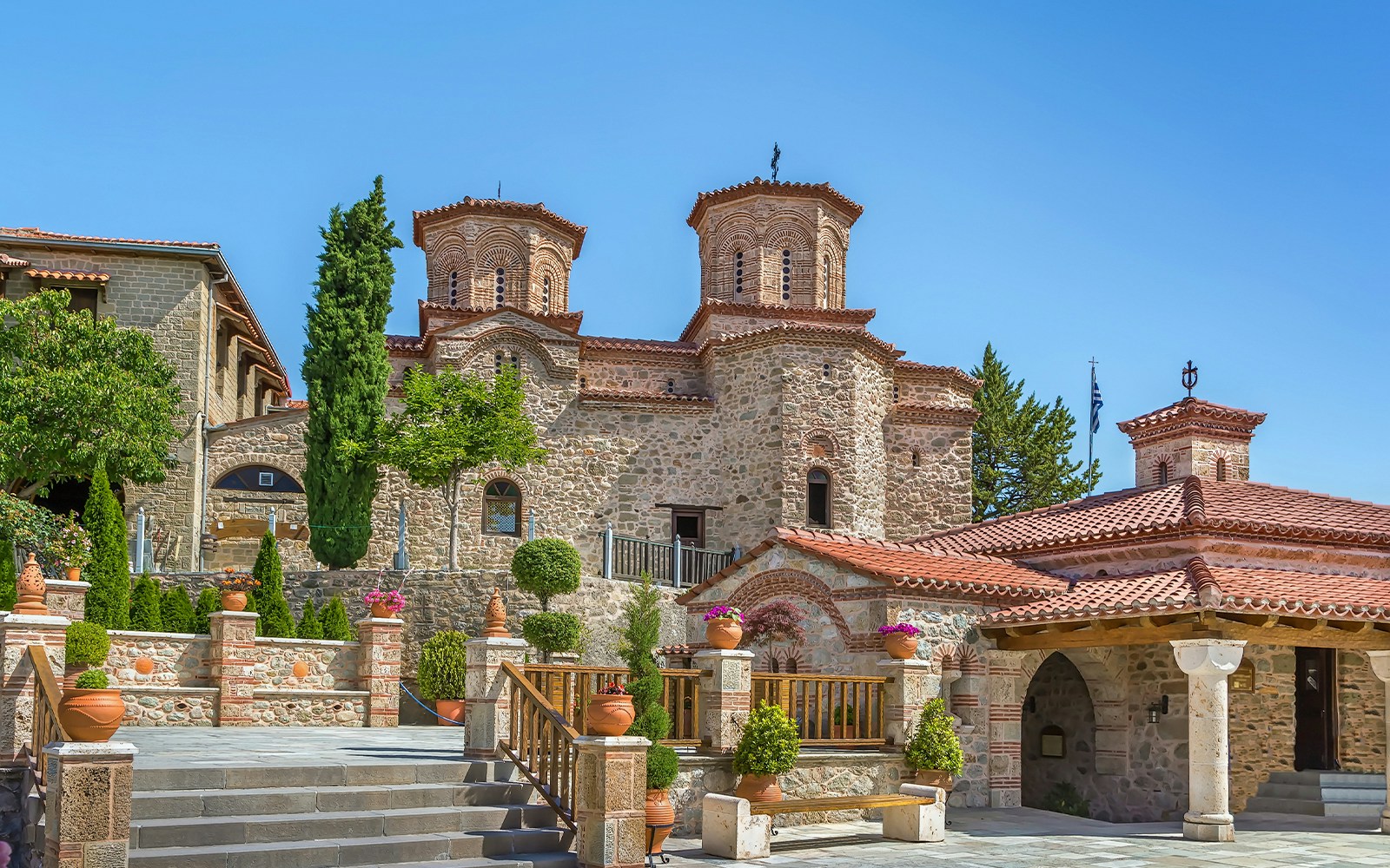 Meteora monastery with stone architecture and lush greenery on a sunny day.