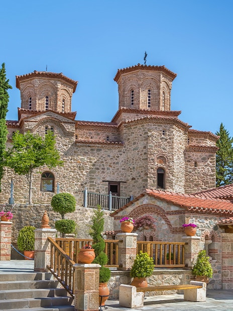 Meteora monastery with stone architecture and lush greenery on a sunny day.