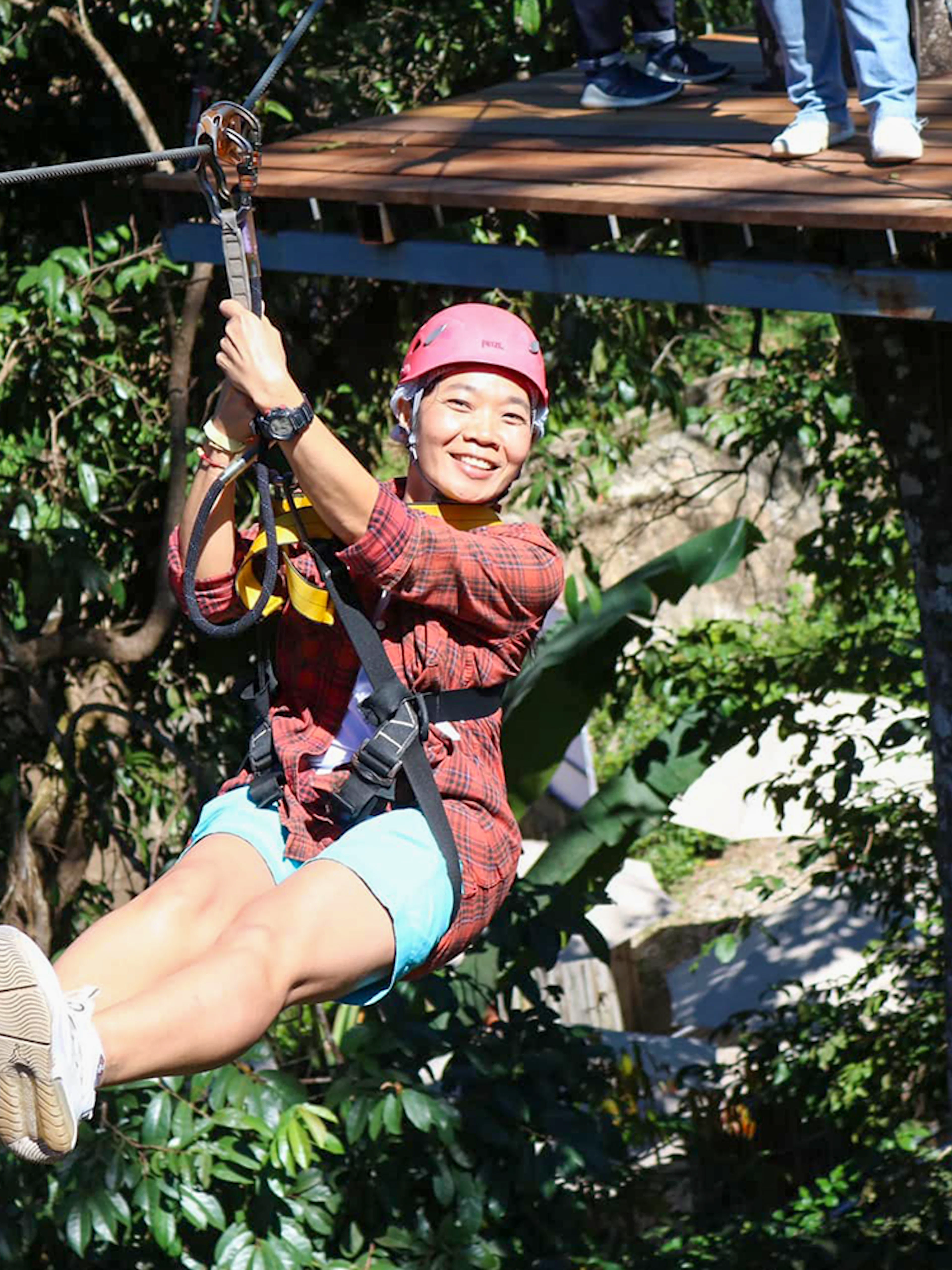 Woman ziplining through lush forest canopy.