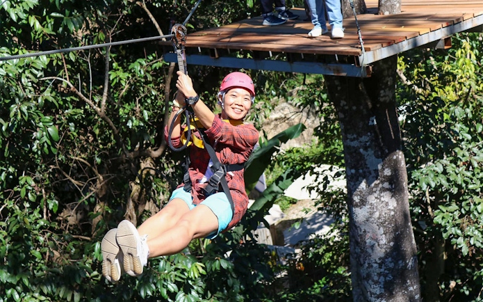 Woman ziplining through lush forest canopy.