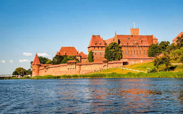 Malbork Castle viewed from across the Nogat River on a sunny day.