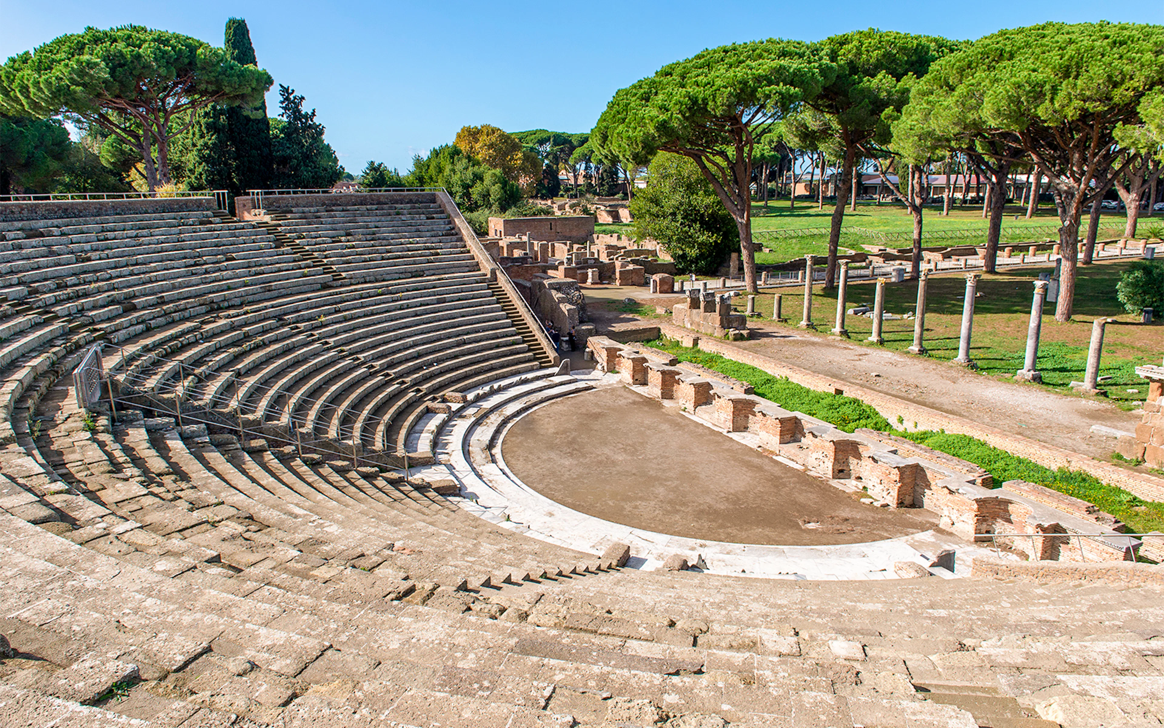 Ancient Roman theater in Ostia Antica with stone seating and surrounding trees.
