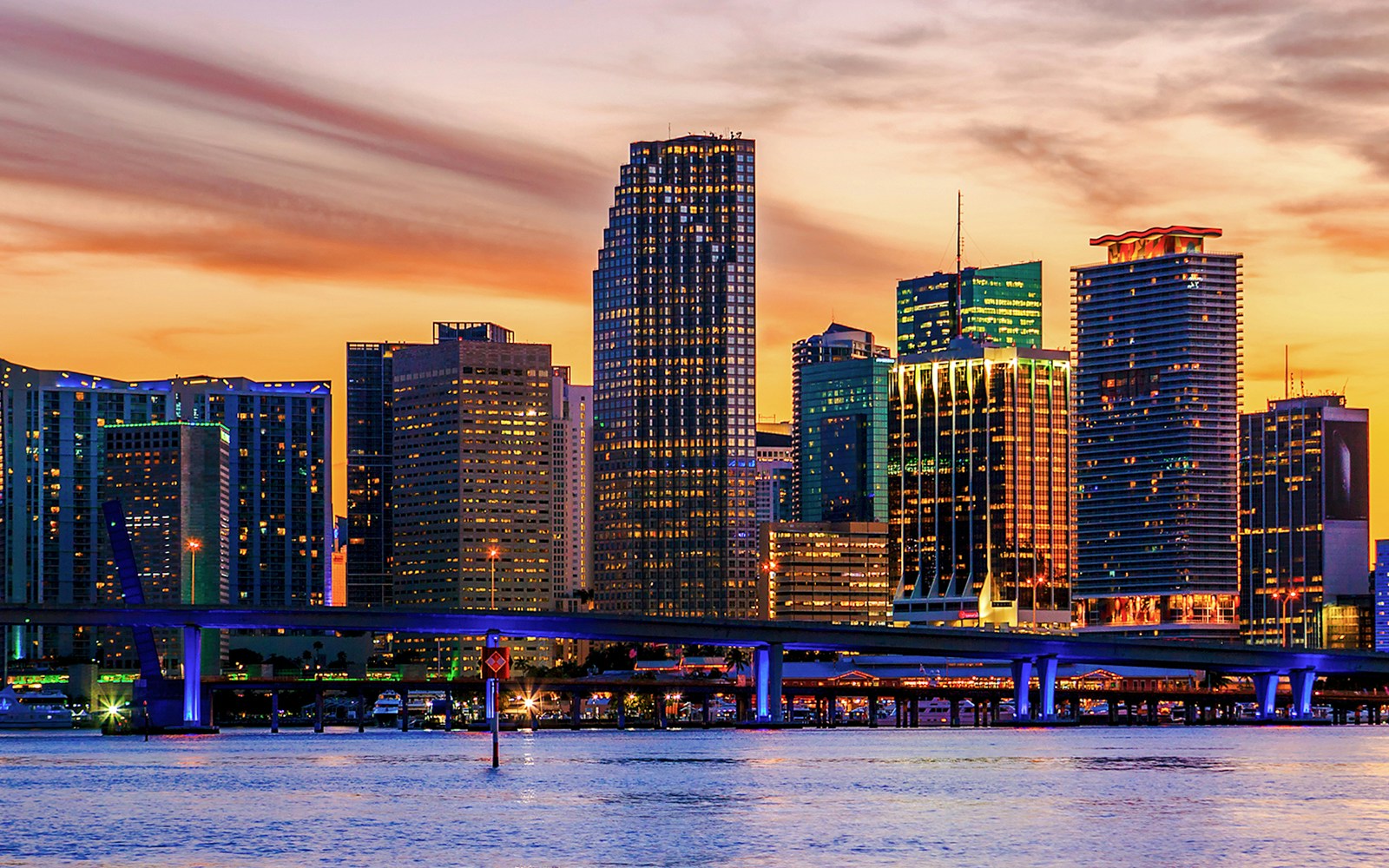 Miami skyline with illuminated buildings and palm trees silhouetted against a vibrant sunset sky.