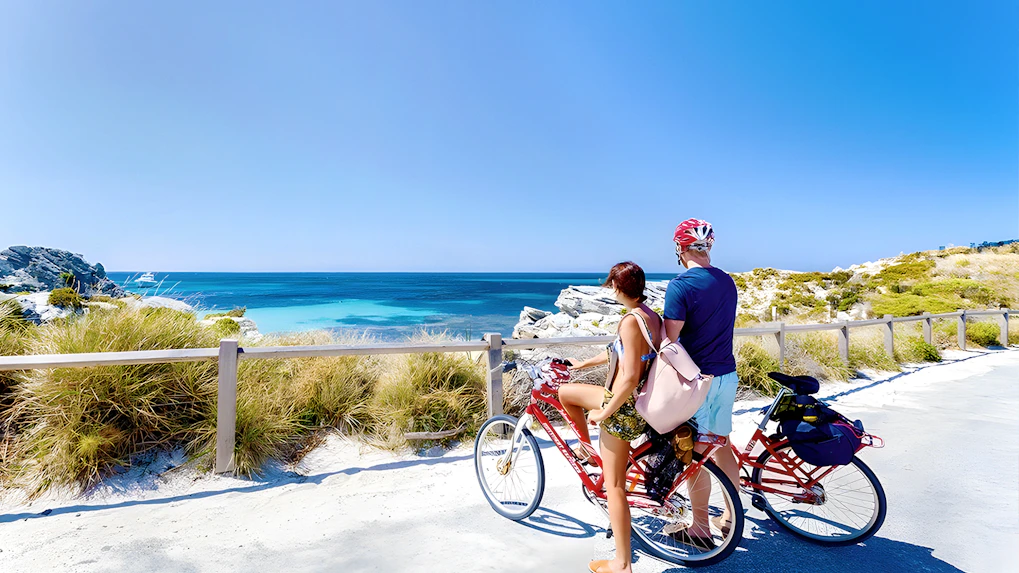 Couple on bikes overlooking the ocean on Rottnest Island, part of the ferry and adventure boat tour.