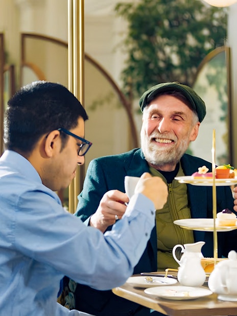 Guests enjoying afternoon tea at Kensington Palace with a tiered tray of pastries.
