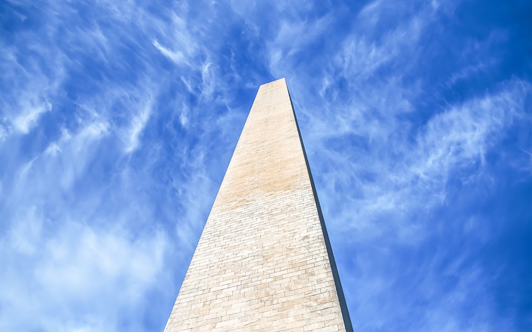 Washington Monument viewed from below against blue sky with clouds.