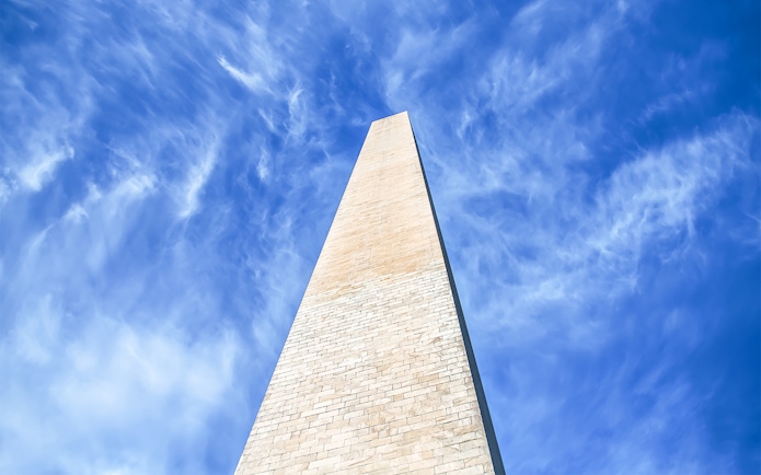 Washington Monument viewed from below against blue sky with clouds.