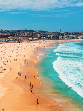 People enjoying the sun and surf at Bondi Beach, Sydney, with cityscape in the background.
