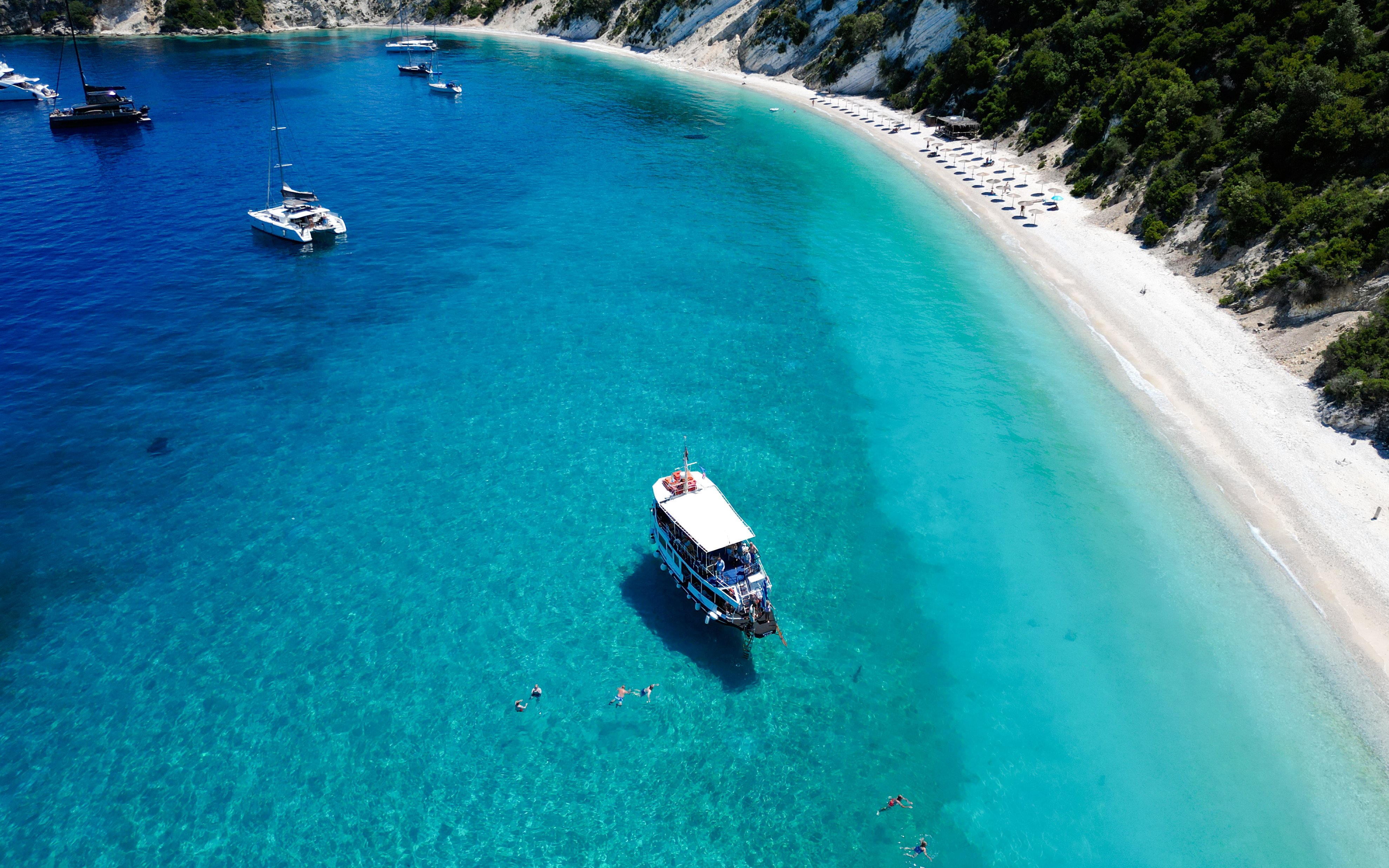 Cruise boat near Gidaki Beach, Ithaca with swimmers in clear waters, Kefalonia, Greece.