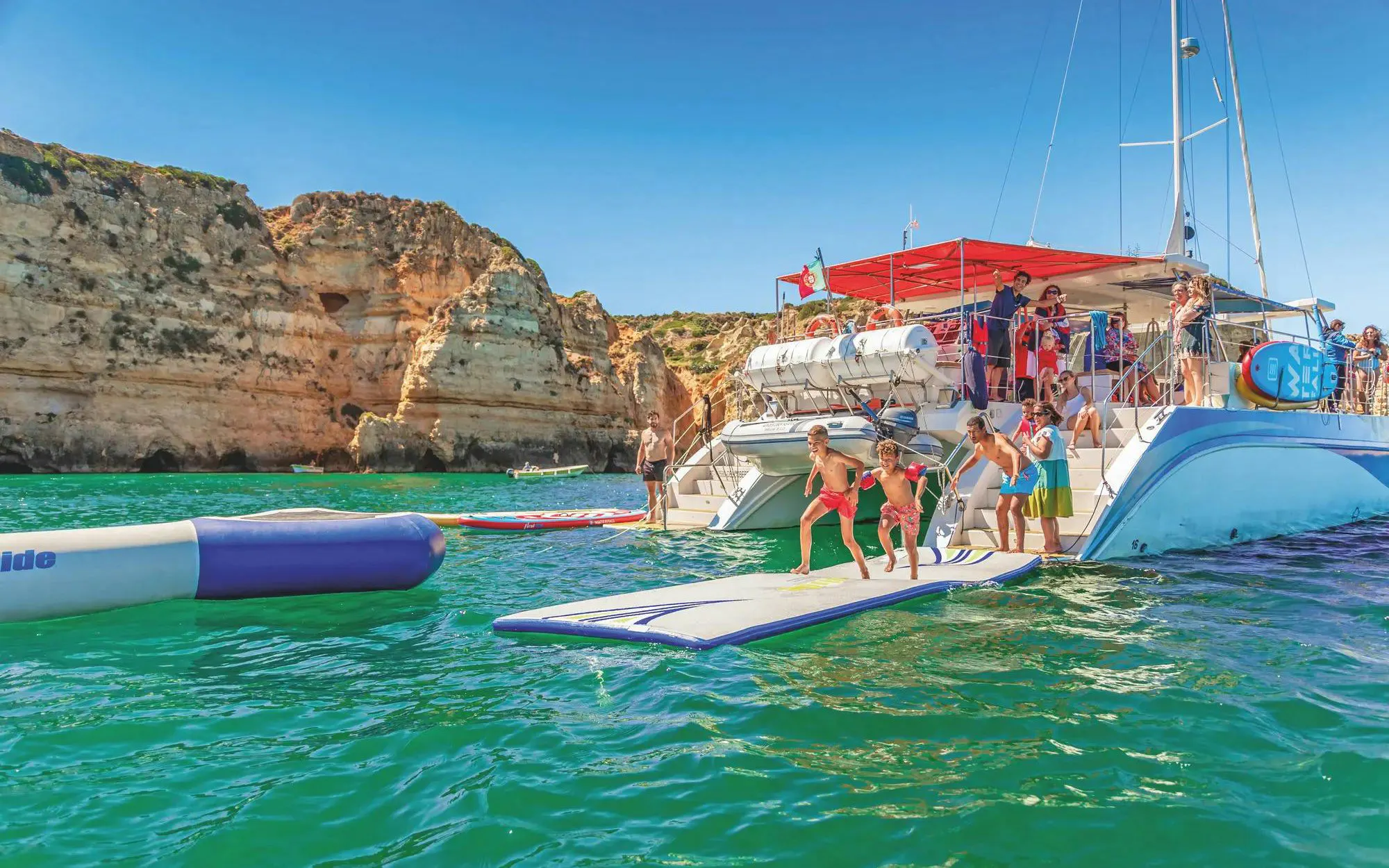 Tourists enjoying inflatable water activities near a boat at Ponta da Piedade, Lagos.