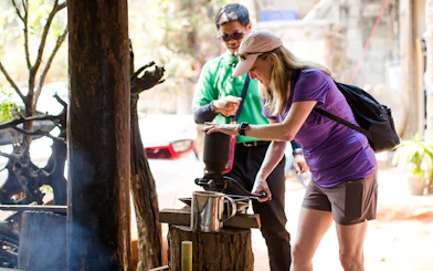 Tourist grinding coffee beans with a traditional grinder on Doi Inthanon tour.