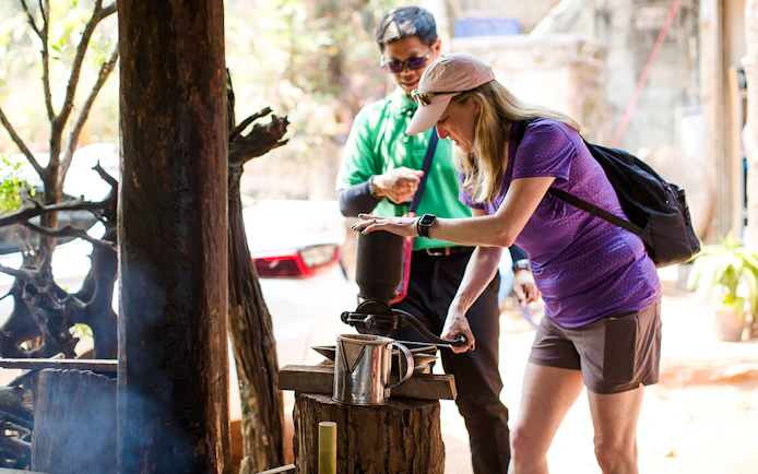 Tourist grinding coffee beans with a traditional grinder on Doi Inthanon tour.