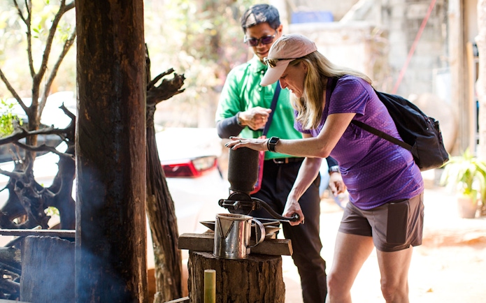 Tourist grinding coffee beans with a traditional grinder on Doi Inthanon tour.