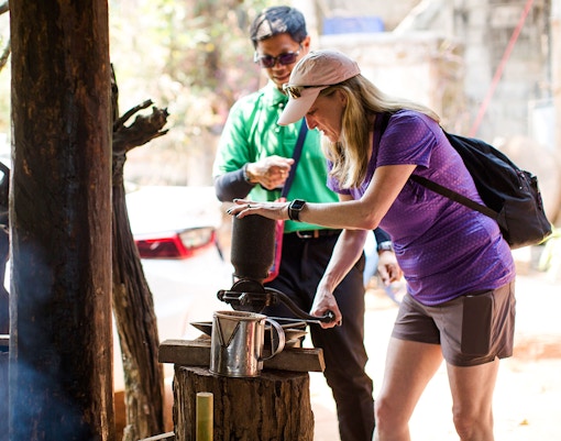 Tourist grinding coffee beans with a traditional grinder on Doi Inthanon tour.