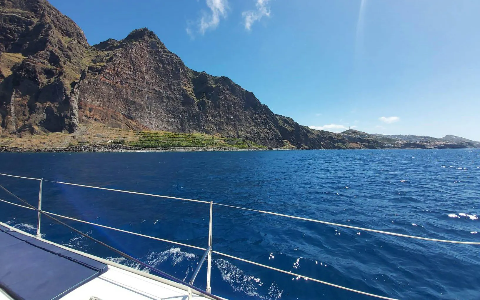 Catamaran sailing near rocky cliffs in Funchal, Madeira.