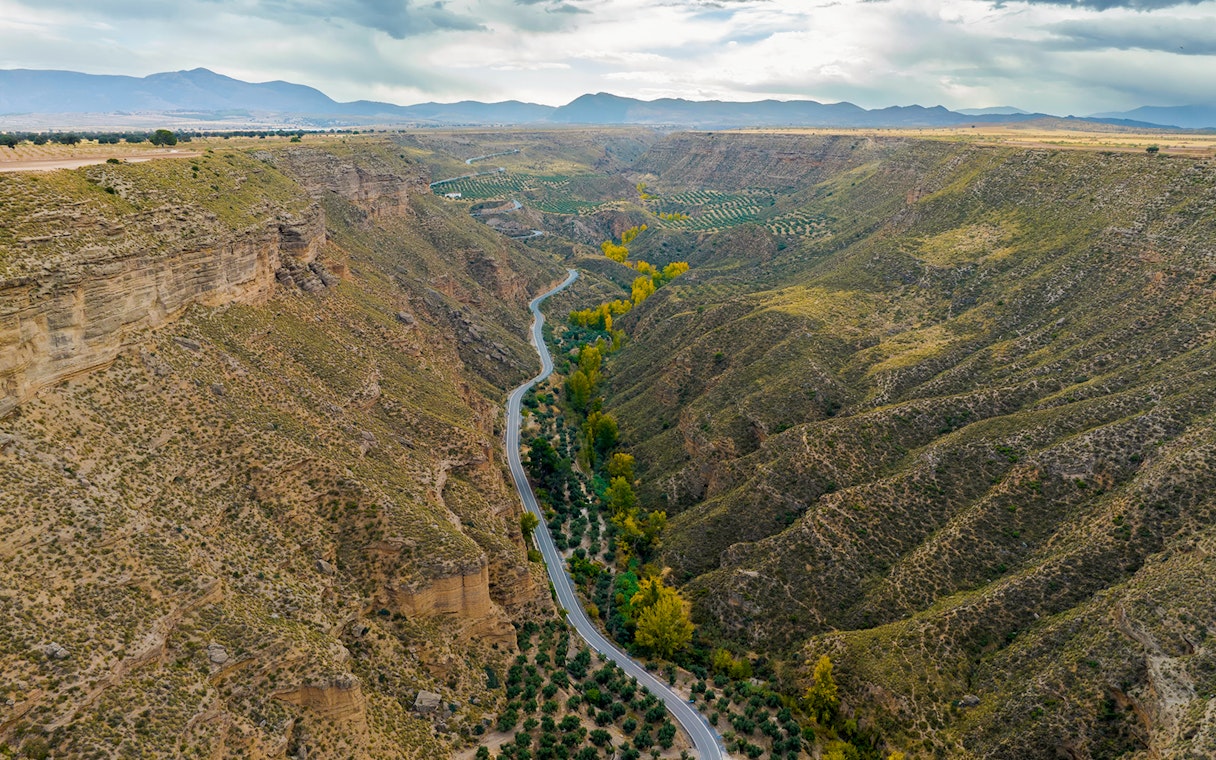 Granada Geopark canyon landscape with winding road and greenery.