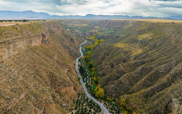 Granada Geopark canyon landscape with winding road and greenery.