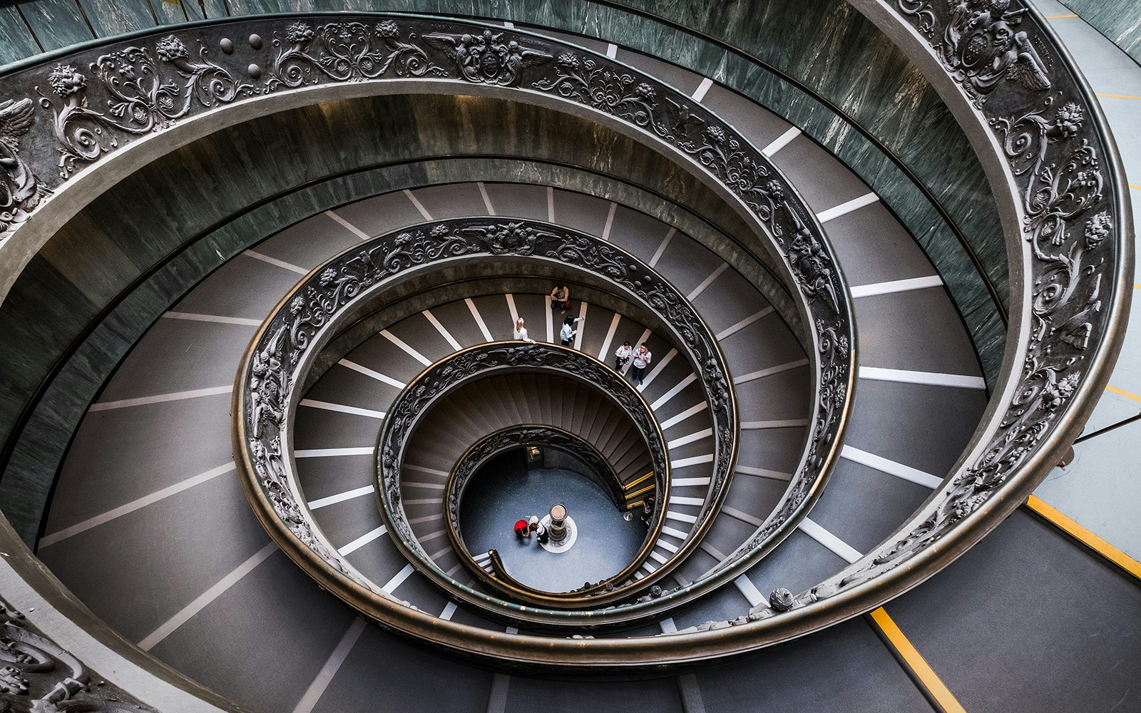 Vatican Museum spiral staircase with ornate railings and visitors descending.