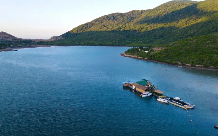 Floating dock with boats on clear water surrounded by lush hills in Nha Trang, Vietnam.