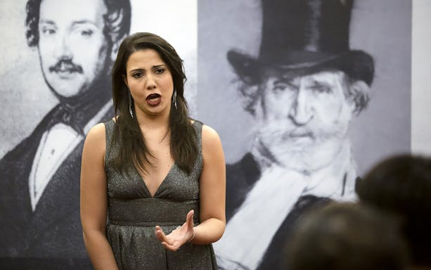 Opera singer performing with portraits of composers in the background.