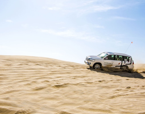 SUV driving through sand dunes on a desert safari in Doha.