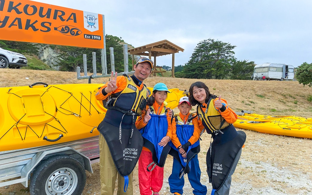 Family ready for kayaking adventure in Kaikoura, New Zealand, standing by yellow kayaks.