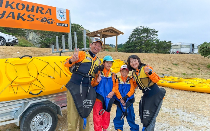 Family ready for kayaking adventure in Kaikoura, New Zealand, standing by yellow kayaks.