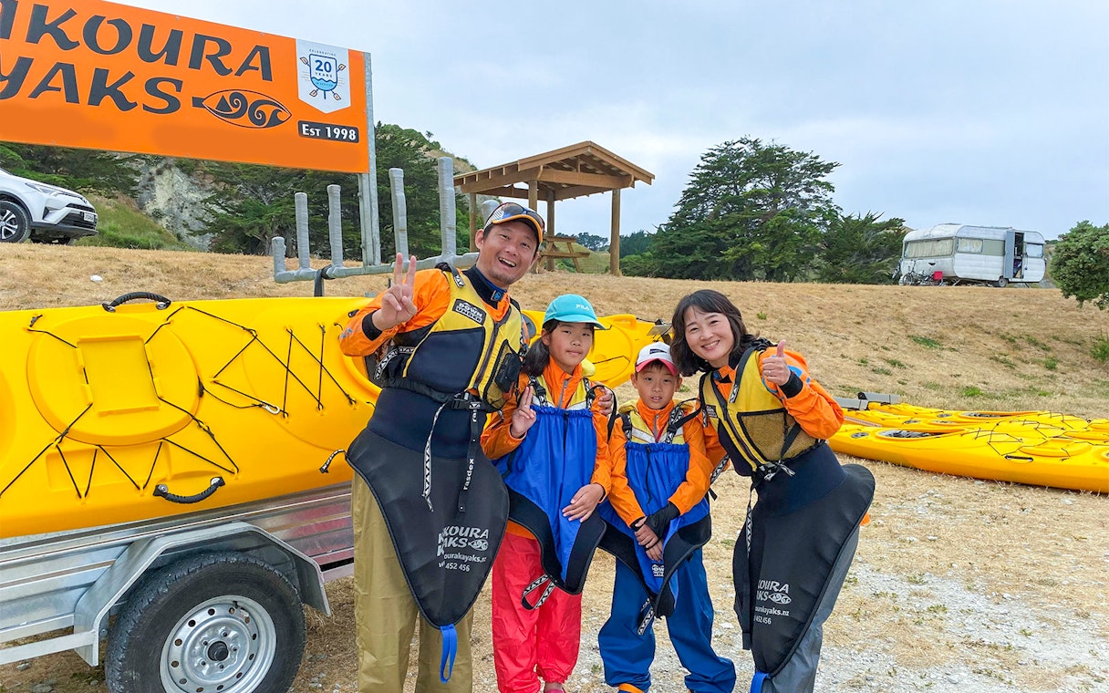 Family ready for kayaking adventure in Kaikoura, New Zealand, standing by yellow kayaks.