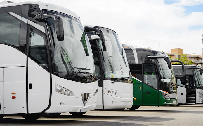 Parked buses at a terminal with buildings in the background.