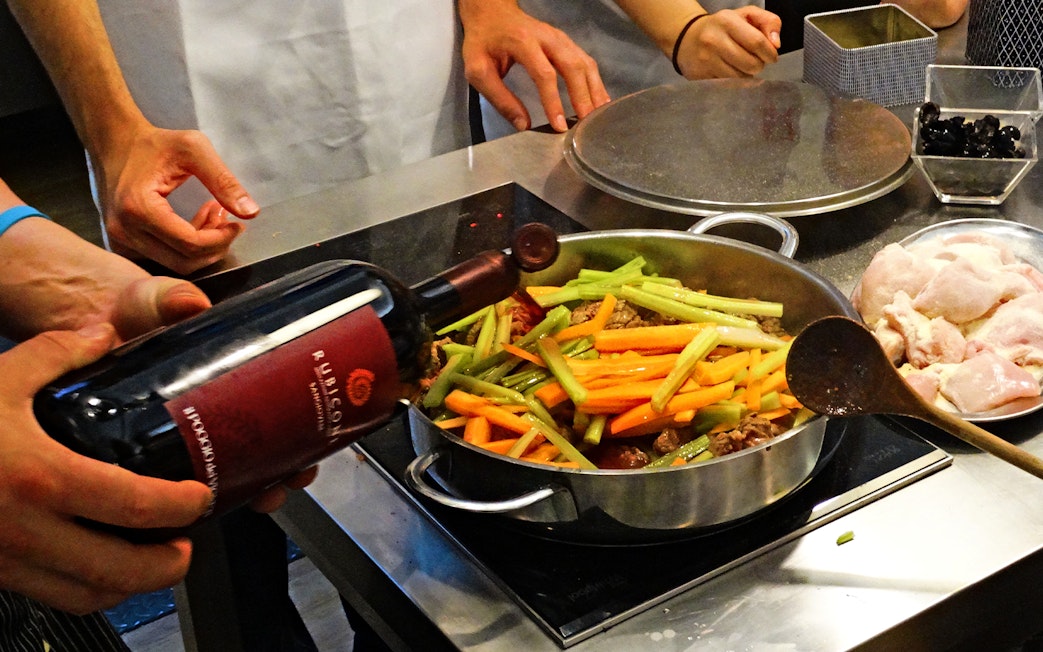 Cooking class in Florence with participants preparing a dish using wine, vegetables, and chicken.