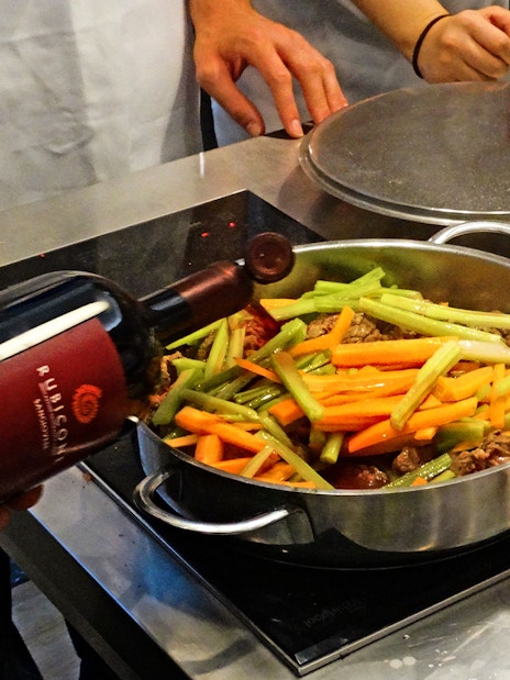 Cooking class in Florence with participants preparing a dish using wine, vegetables, and chicken.