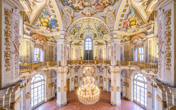 Ornate interior of a historic palace in Turin, featuring frescoed ceilings and a grand chandelier.