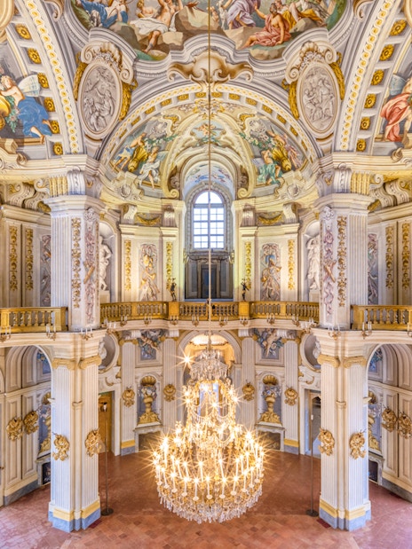 Ornate interior of a historic palace in Turin, featuring frescoed ceilings and a grand chandelier.