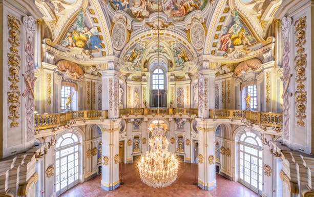 Ornate interior of a historic palace in Turin, featuring frescoed ceilings and a grand chandelier.