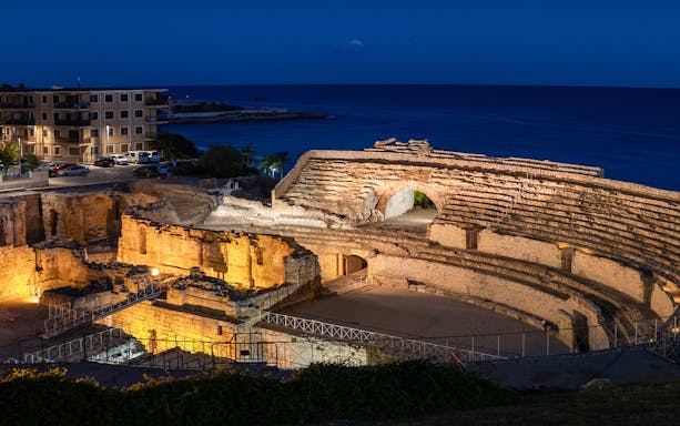 Ancient Roman amphitheater by the sea illuminated at night, Tarragona, Spain.