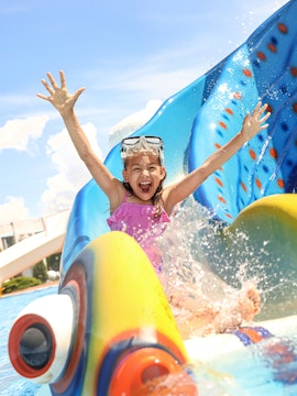 Little girl sliding down a colorful water slide at a water park.