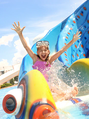 Little girl sliding down a colorful water slide at a water park.