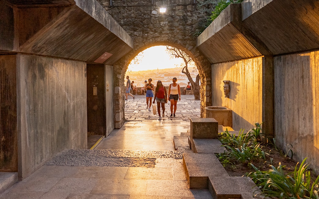 Visitors walking through an archway at St George's Castle during sunset.
