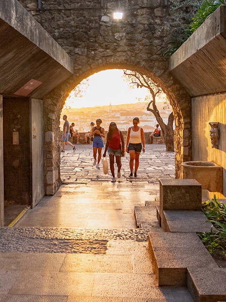 Visitors walking through an archway at St George's Castle during sunset.